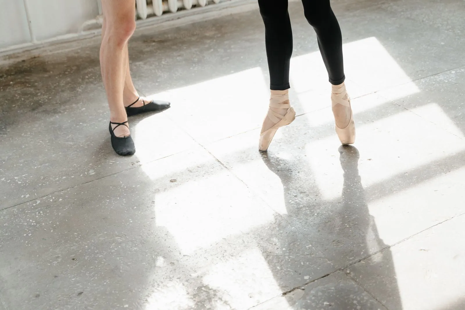 Close-up of ballet dancers practicing in a sunlit studio, showcasing technique and grace.